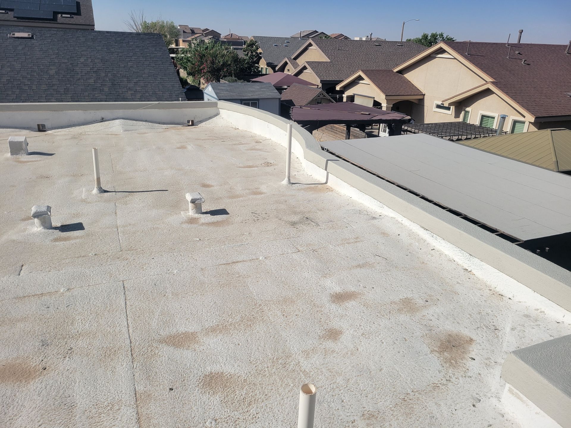 Flat white rooftop with vents and skylights overlooking neighboring houses in a suburban area