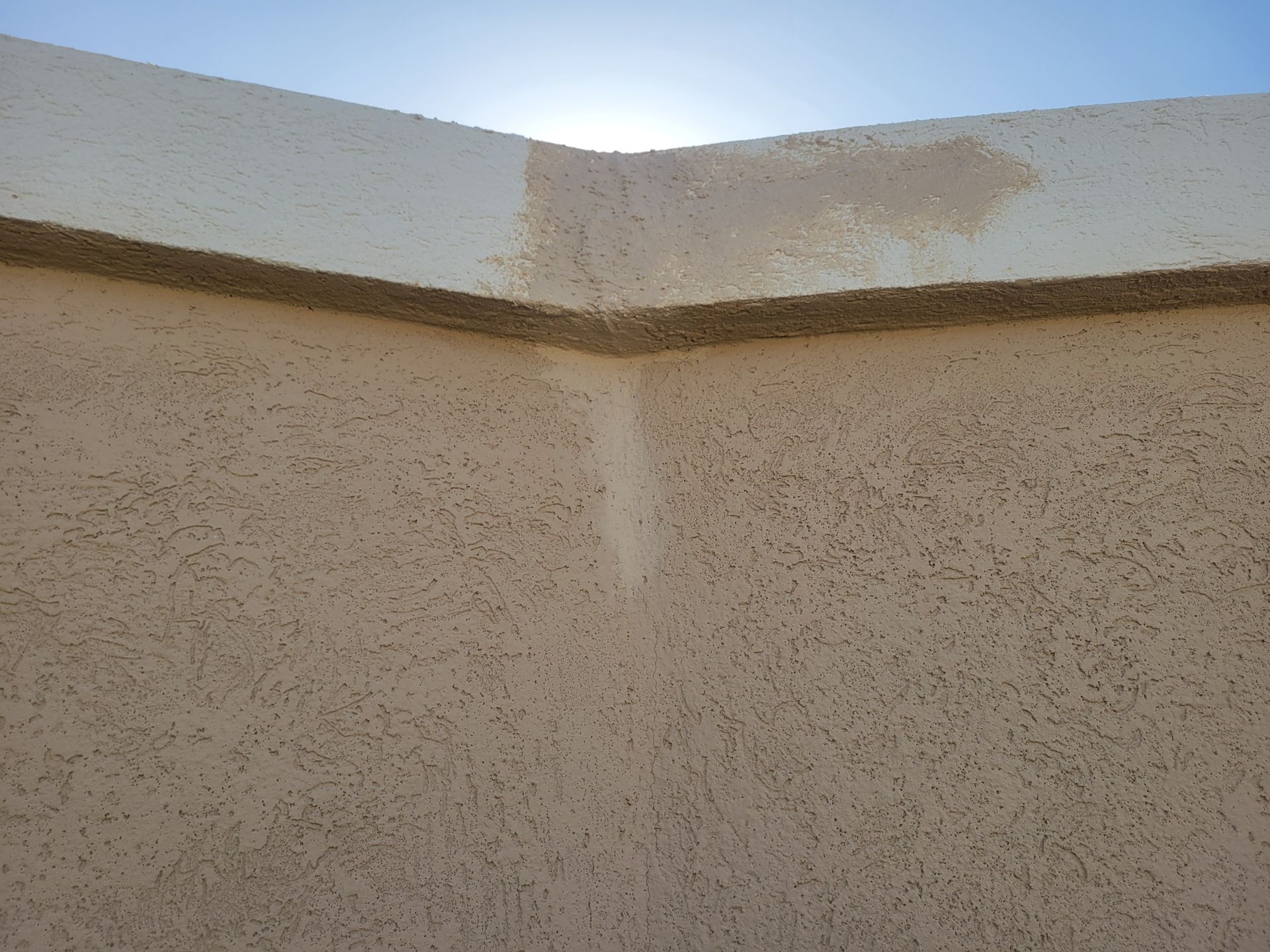 Corner of a beige stucco wall with a white-painted top edge and a vertical water stain.