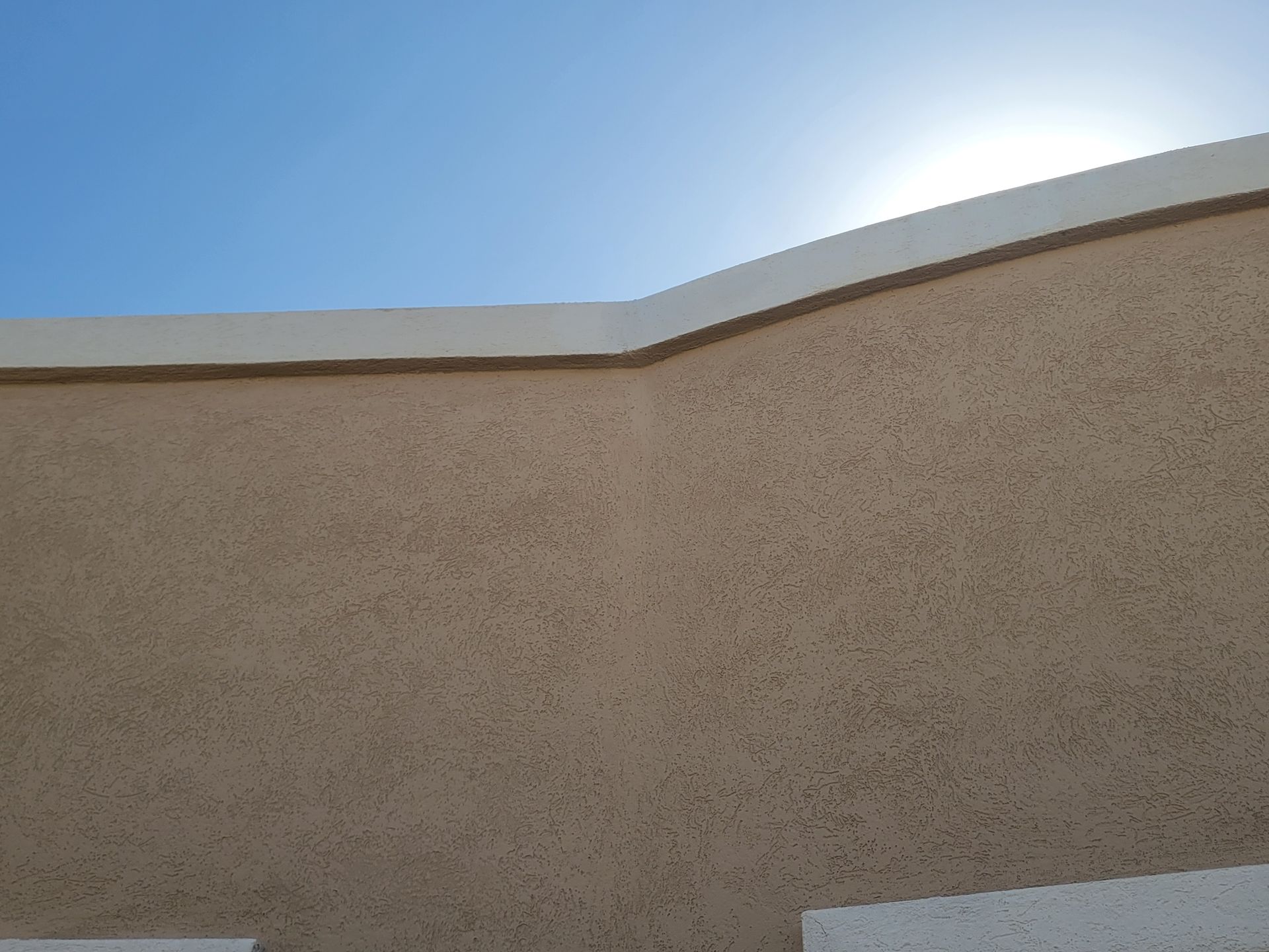 Beige stucco wall with a curved roofline against a bright blue sky