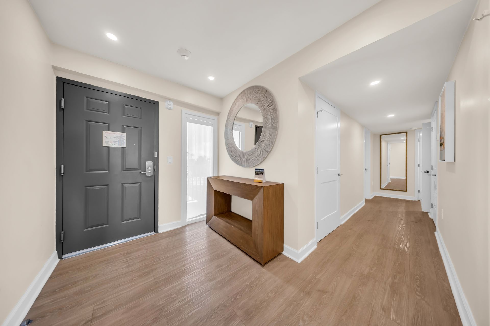 Bright hallway entryway with dark front door, wood floors, white walls, mirror, and console table