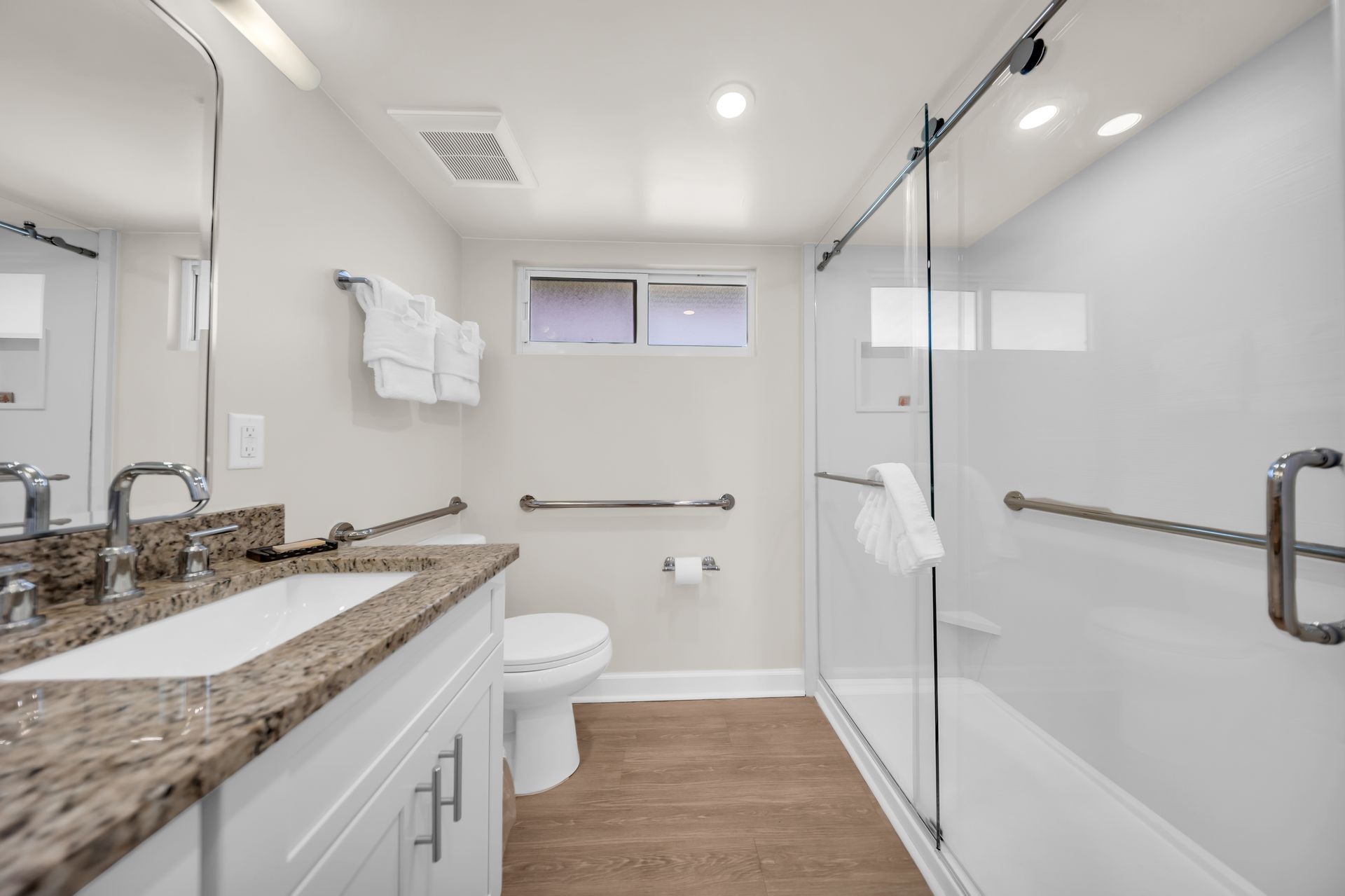 Bright modern bathroom with granite vanity, toilet, and glass walk-in shower with white tile.