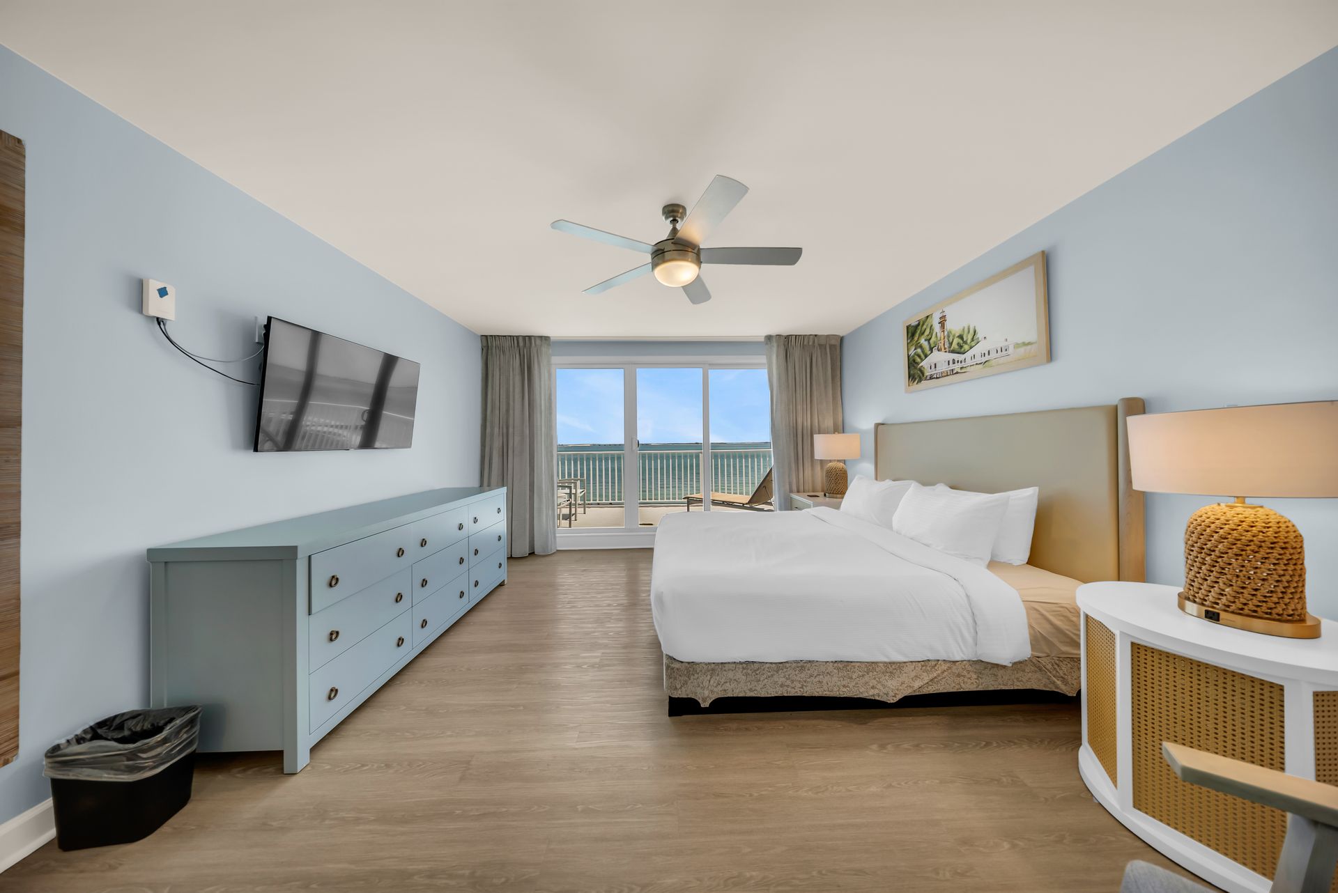 Bright bedroom with a king bed, blue dresser, wall TV, and balcony doors overlooking mountains.