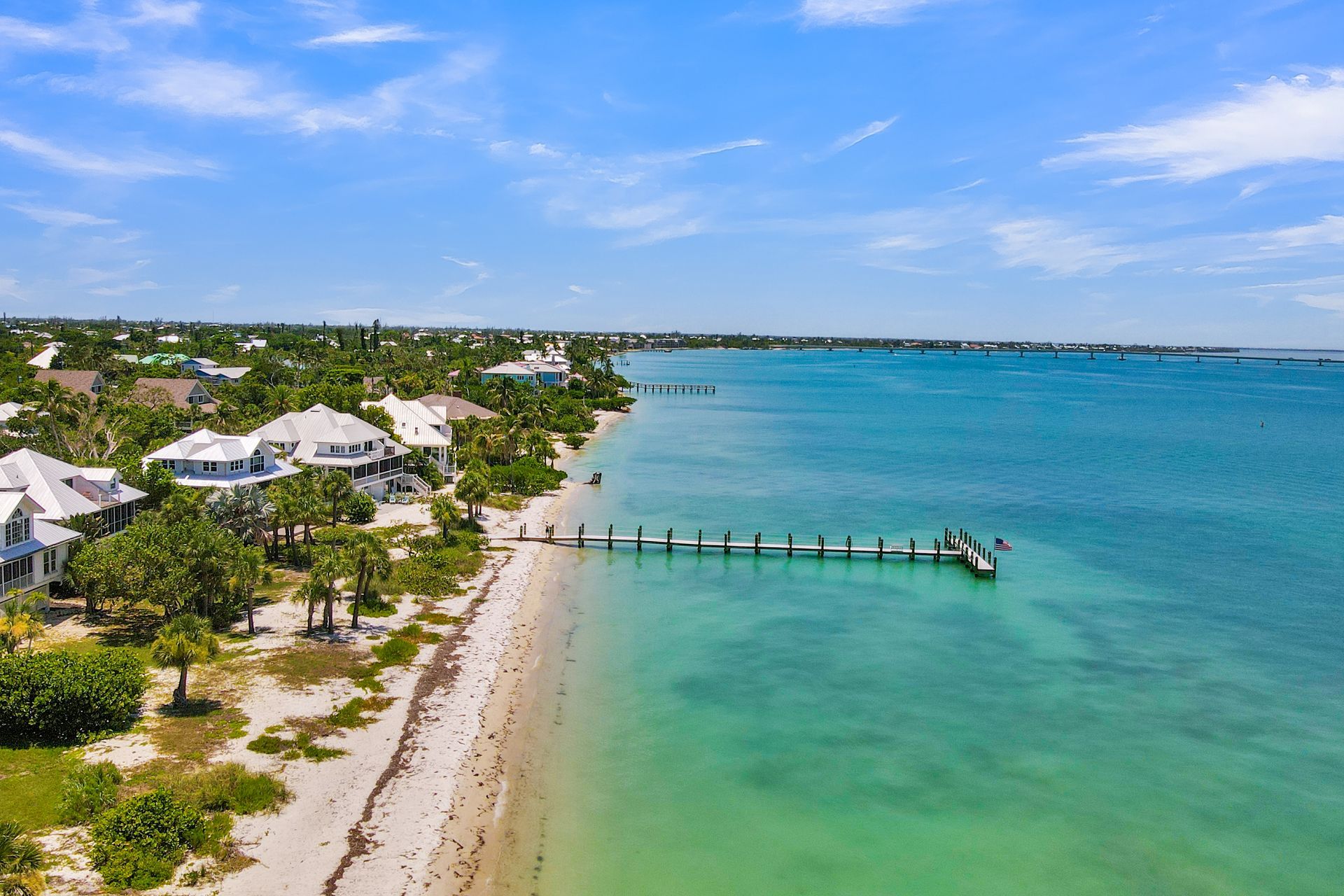 Tropical beach with white villas, turquoise water, and a wooden pier under a blue sky