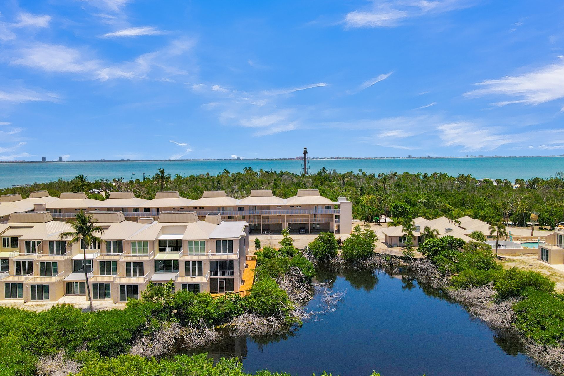 Waterfront resort condos beside a lagoon under a bright blue sky, with palm trees and ocean in the distance