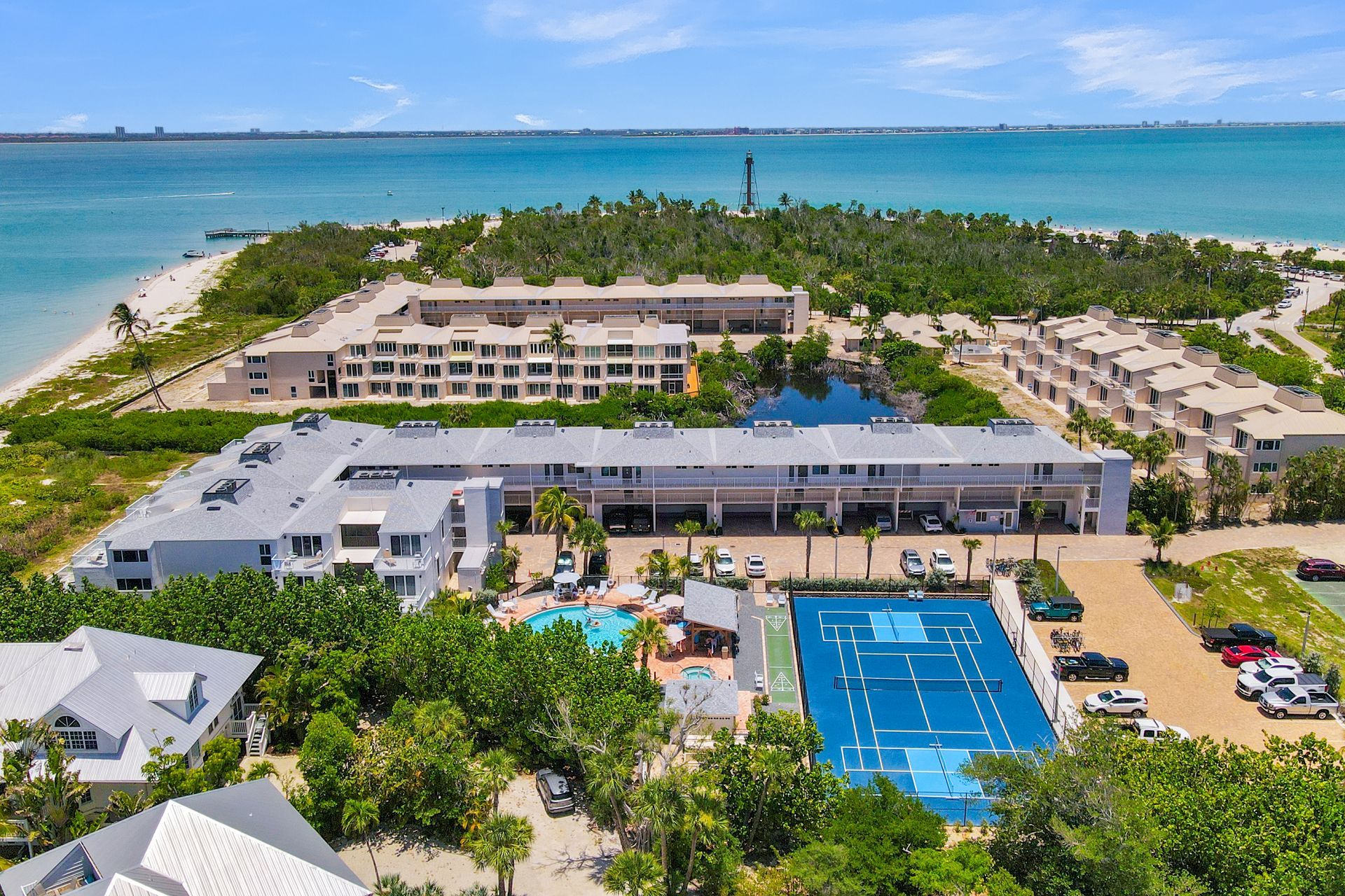 Aerial view of a beachfront resort with blue tennis courts, pools, and palm trees by the ocean