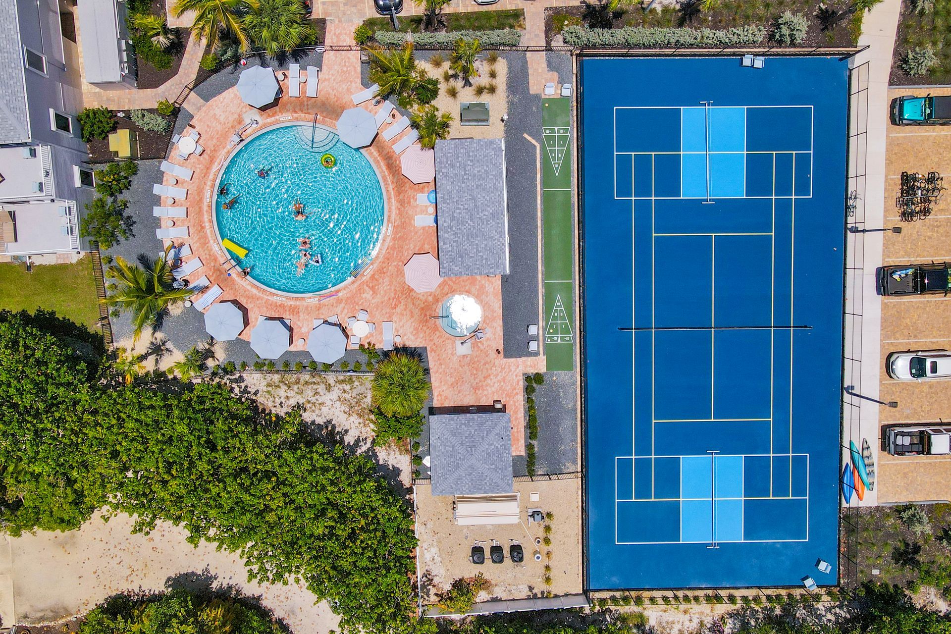 Aerial view of a blue tennis court beside a circular swimming pool in a resort courtyard Aerial view of a blue tennis court beside a circular swimming pool in a resort courtyard