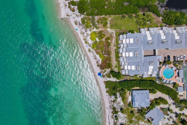 Aerial view of a turquoise beach beside a resort with pools and white buildings Aerial view of a turquoise beach beside a resort with pools and white buildings