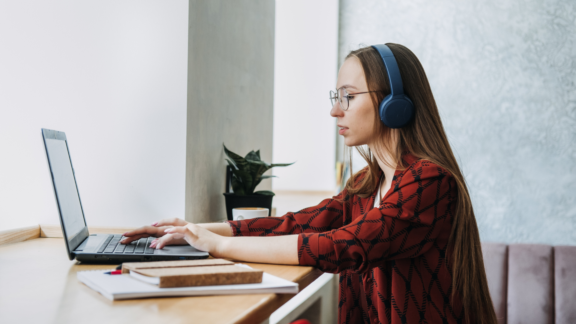 Woman with glasses and headphones working on laptop at a desk.
