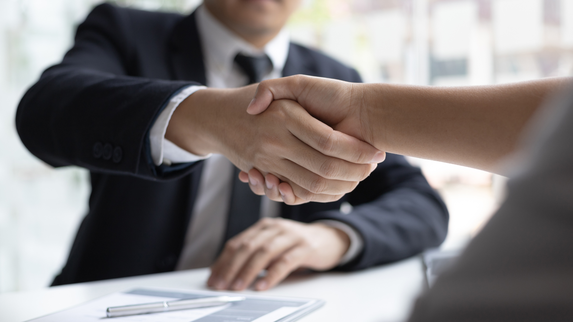 Man in suit shaking hands with a person; office setting, agreement.