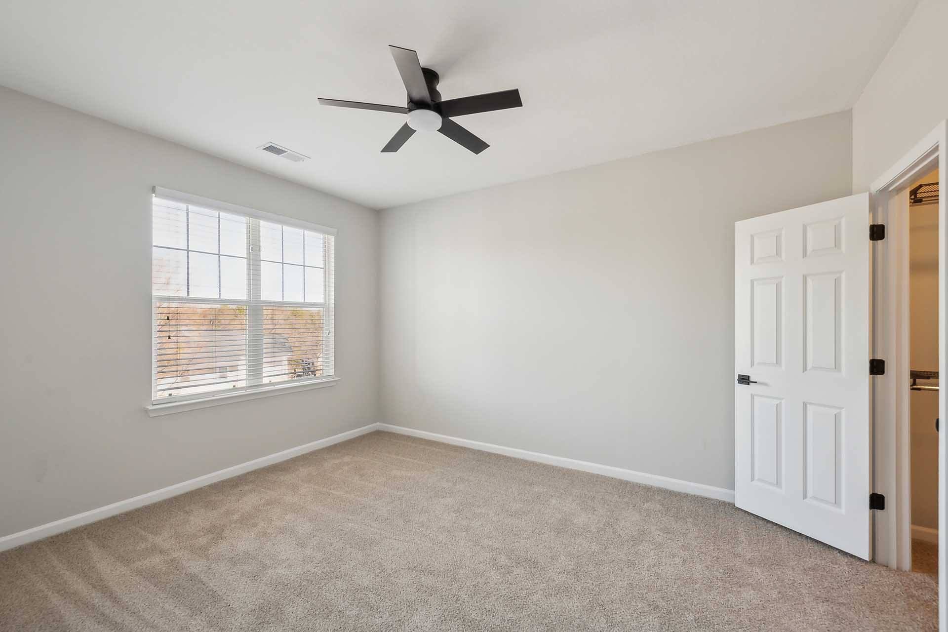 A room with a ceiling fan and a window with blinds.