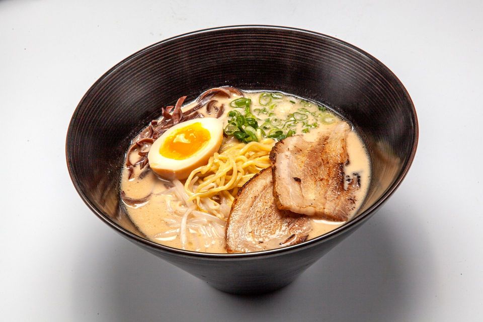 Bowl of ramen with sliced pork, soft-boiled egg, and green onions in creamy broth