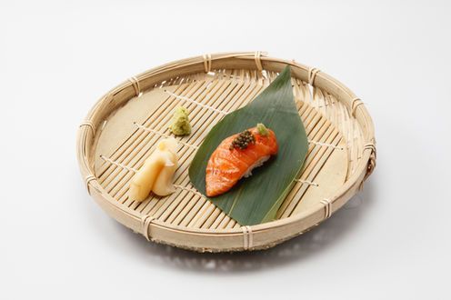 Sushi pieces on a bamboo tray, including salmon nigiri and a roll with wasabi and pickled ginger