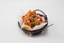 Basket of crispy fried chicken with lemon wedge and herbs on white background