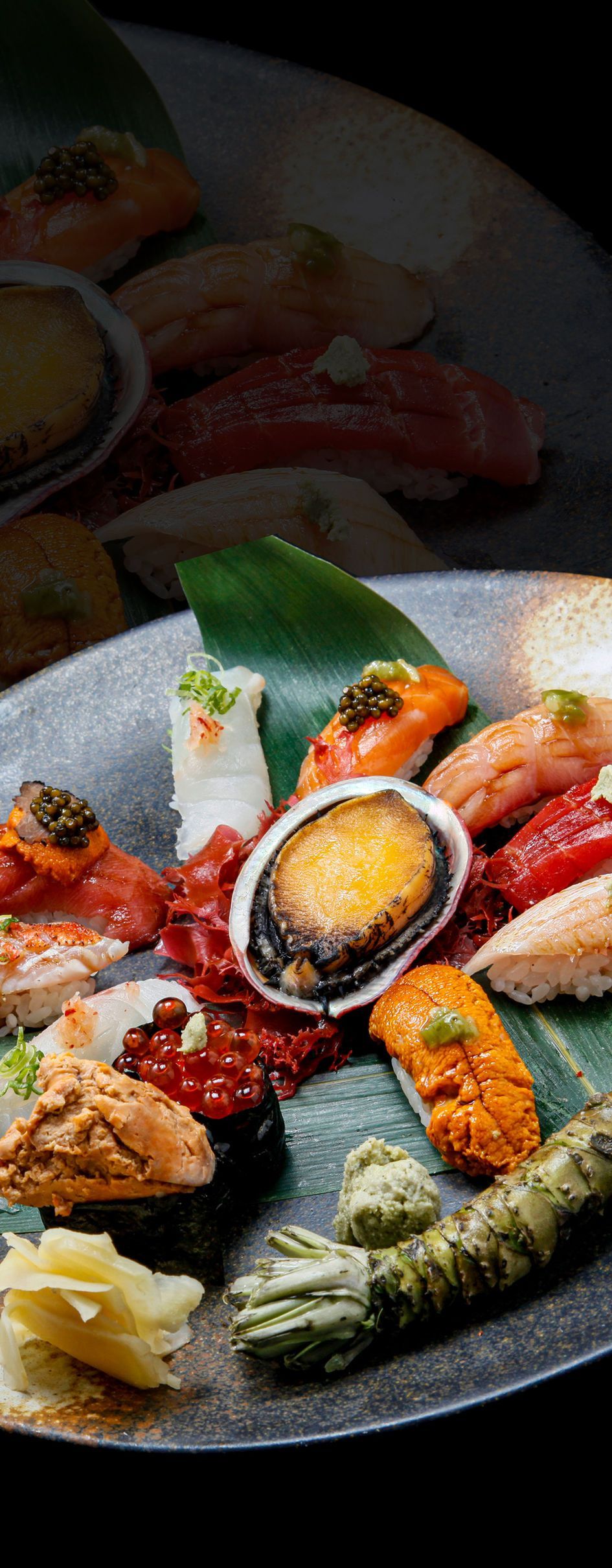 Assorted sushi on a dark plate, with salmon, tuna, rolls, and a halved egg on rice.