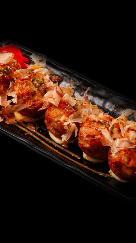 Grilled skewered meat glazed with sauce and topped with chopped herbs on a black tray