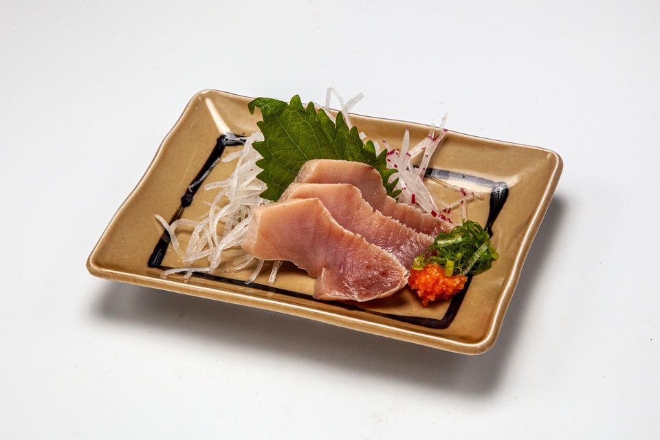 Plate of sashimi with sliced raw fish, shredded daikon, green garnish, and wasabi on a tan platter