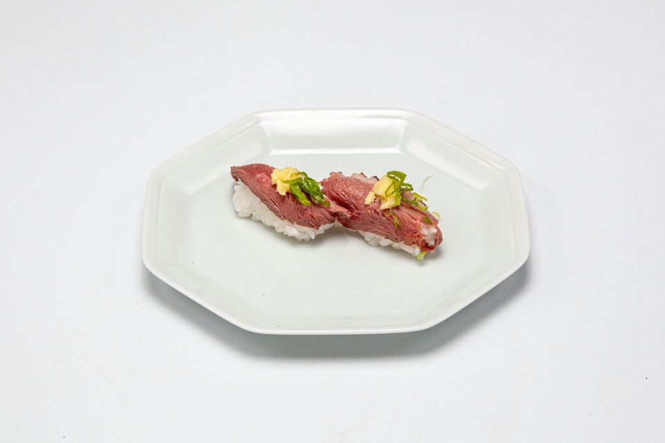 Two slices of seared meat garnished with greens on a white octagonal plate
