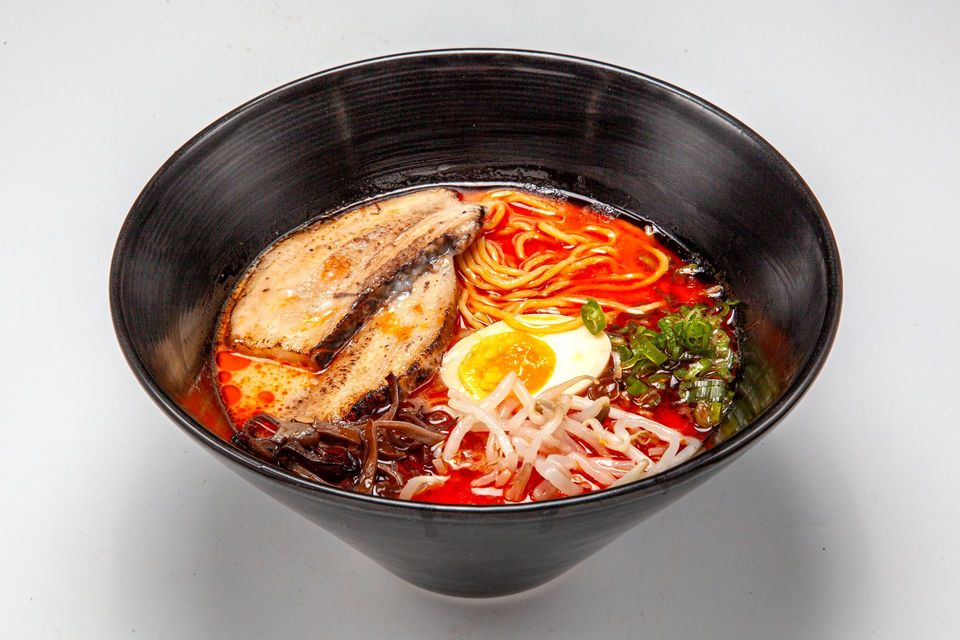Black bowl of ramen with noodles, sliced meat, egg, and green onions in broth