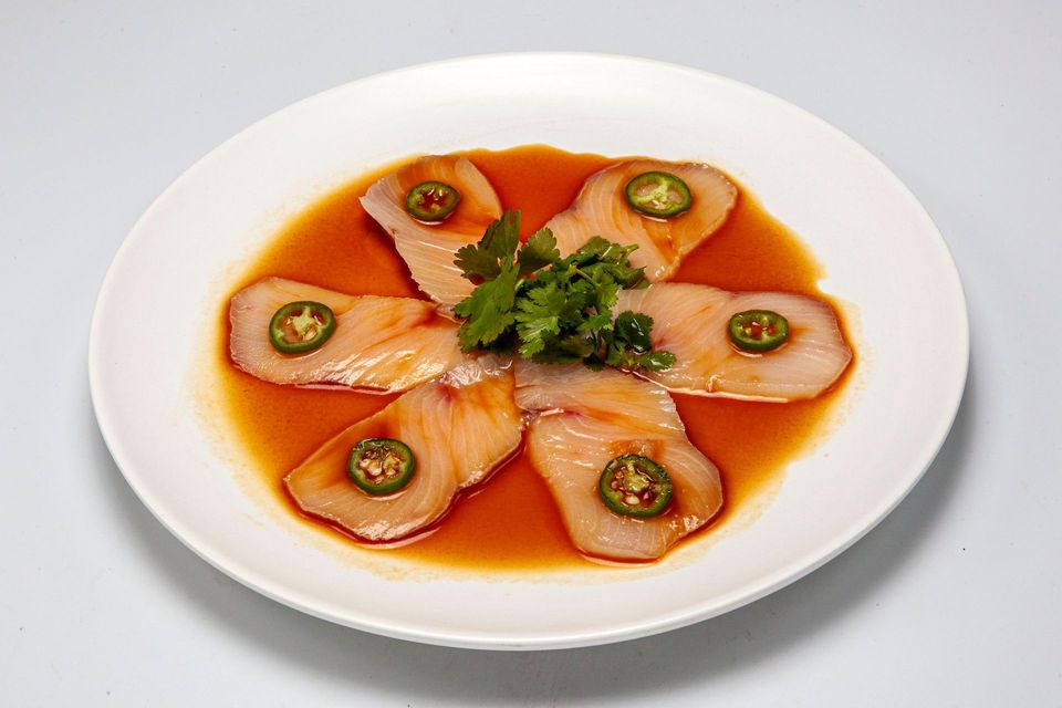 Sliced salmon sashimi on a white plate with orange sauce, garnished with parsley and jalapeño slices