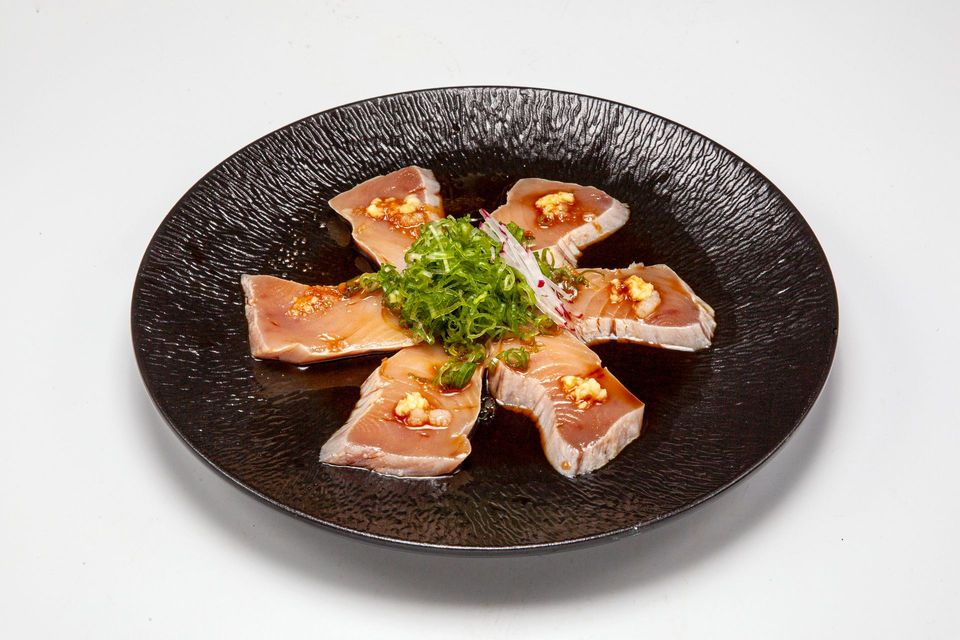 Sliced roasted fish on a black plate, garnished with green herbs and sauce