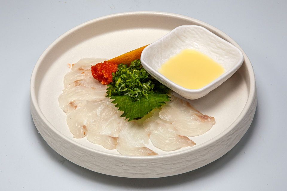 Plate of thin white sashimi with green garnish, red roe, and a small dish of yellow sauce