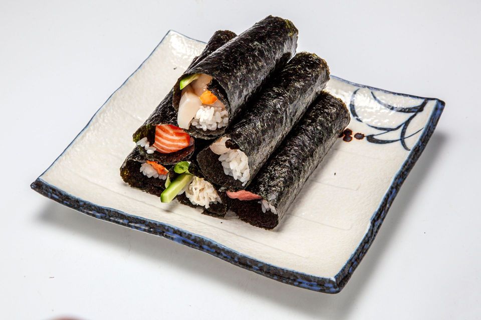 Sushi rolls wrapped in dark seaweed on a square white plate, garnished with vegetables