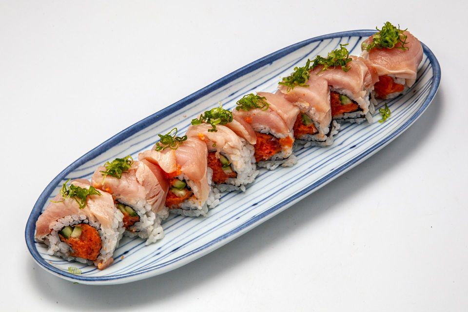 Sushi rolls topped with sliced salmon on a white oval plate, garnished with herbs
