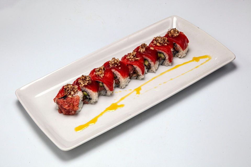 Sushi roll topped with red sauce and gold flakes on a white rectangular plate with yellow drizzle