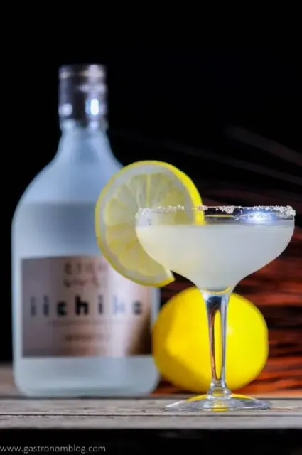 Cocktail glass with lemon slice beside a frosted bottle on a wooden table