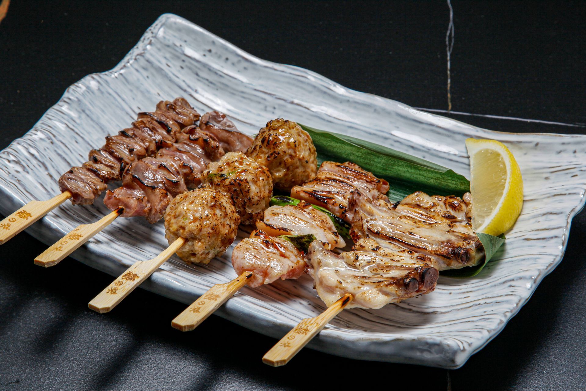 Assorted grilled meat skewers and slices on a white plate with lemon wedge and green garnish