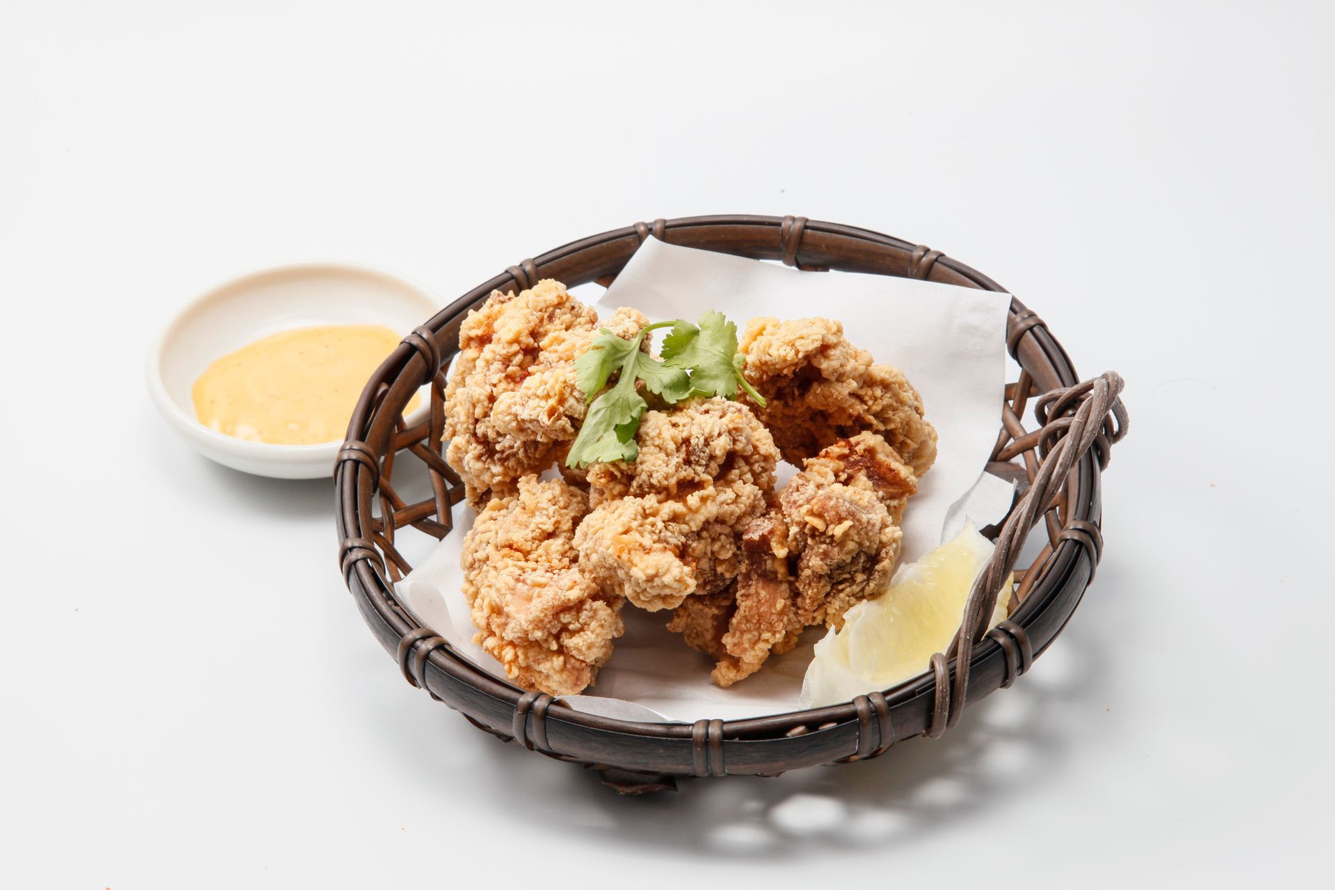 Fried chicken in a wicker basket with dipping sauce on a white background