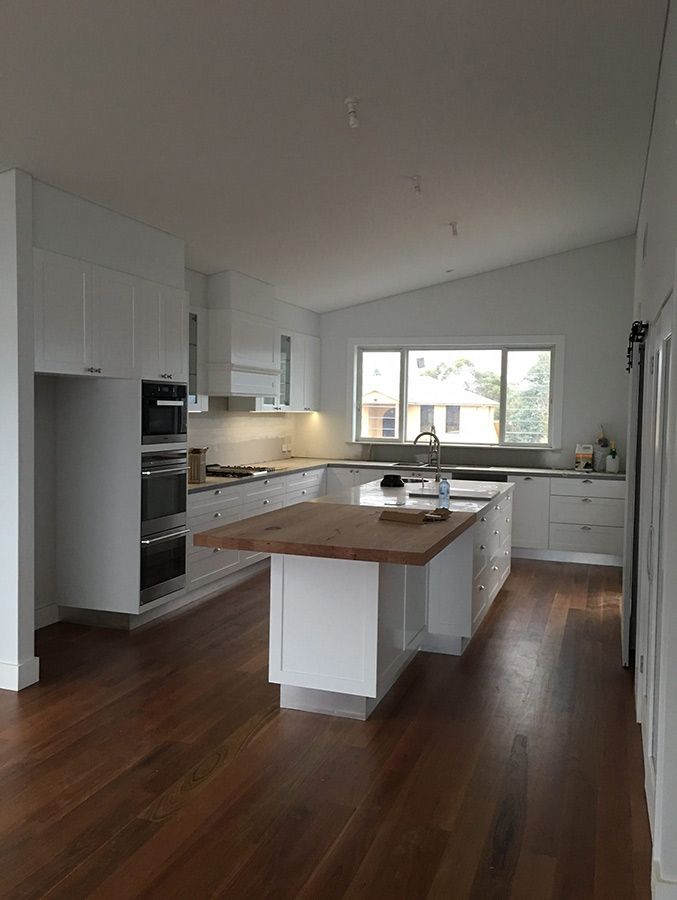 A Kitchen With White Cabinets and Wooden Floors and a Large Island in the Middle — Allnew Kitchens in Charmhaven, NSW