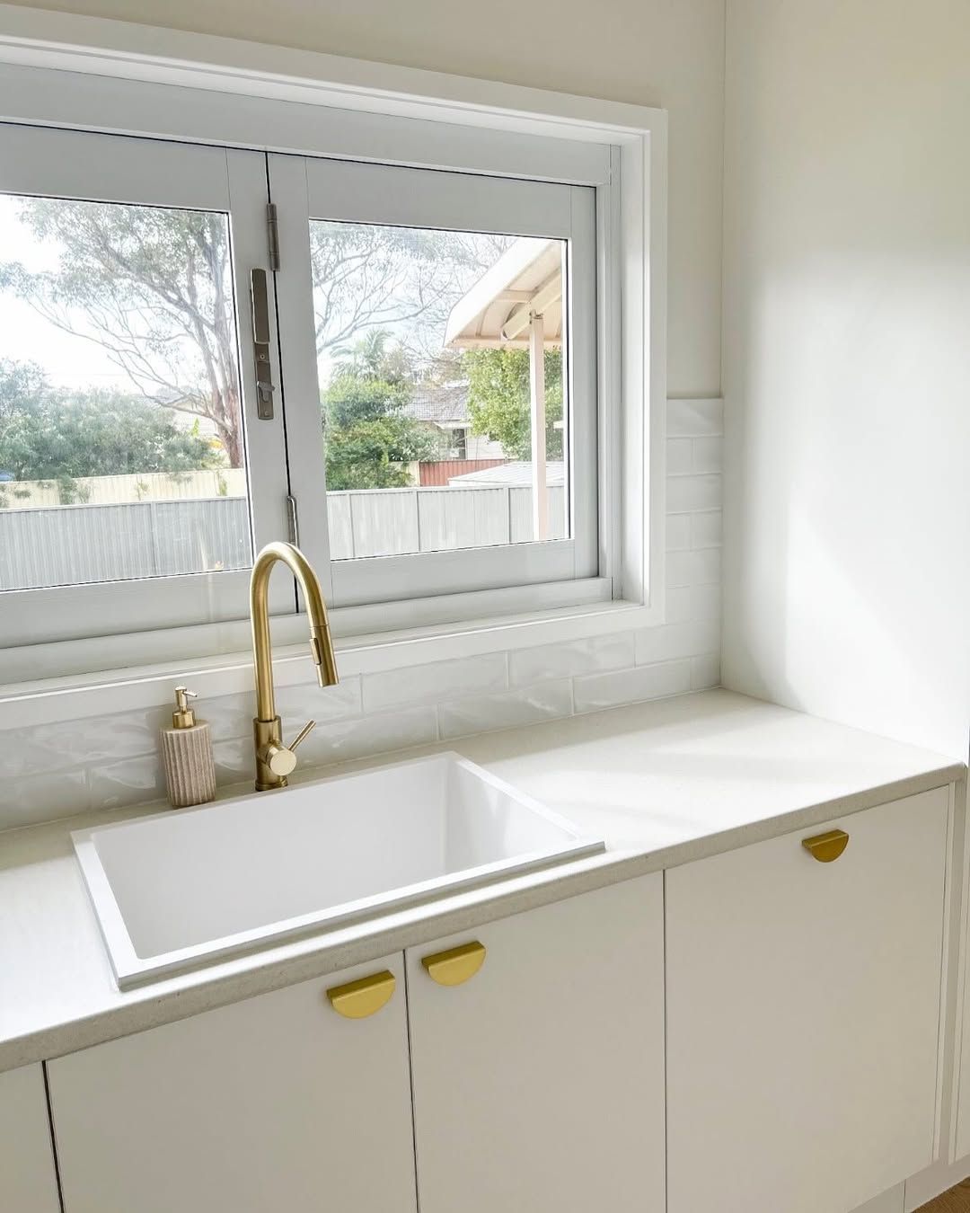 White laundry room with sink, golden faucet, and hardware, and a window overlooking a yard. — Allnew Kitchens in Charmhaven, NSW