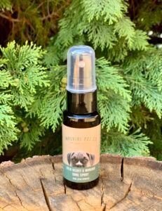 Deer Velvet and Manuka Oral Spray bottle on wooden surface surrounded by greenery, highlighting natural pet health product.