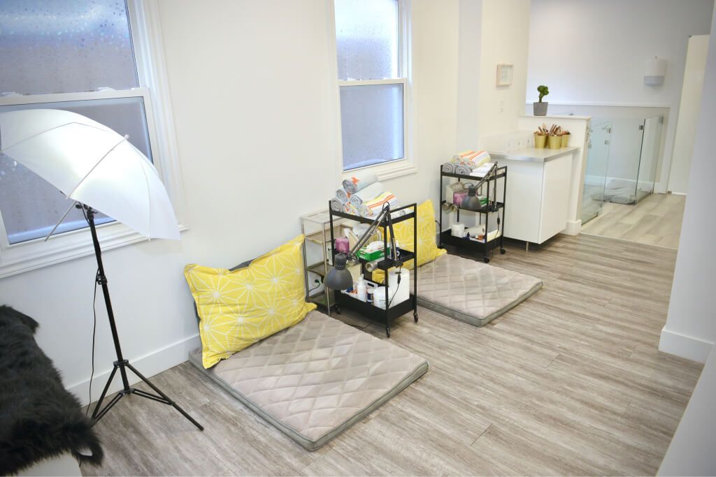 Bright room with two pet beds, black shelving cart, umbrella light, and white cabinet on wood flooring