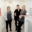 Three smiling staff members stand in a bright hallway, wearing gray and black uniforms.
