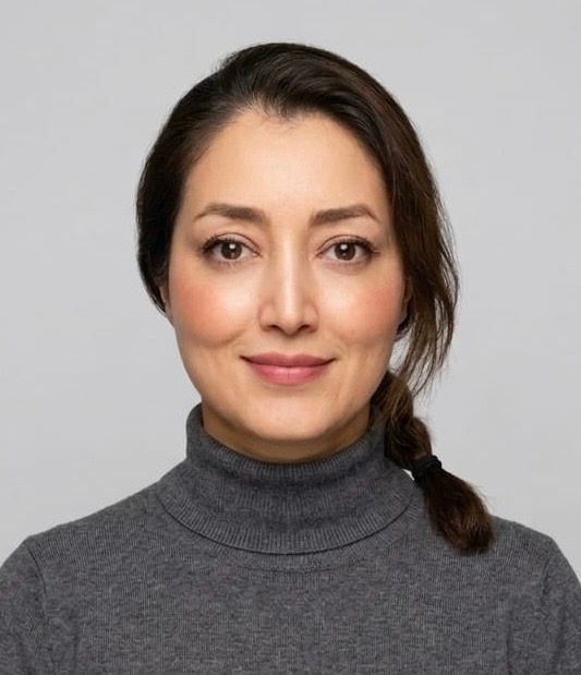 Portrait of a person in a gray turtleneck, facing forward with a slight smile on a plain background.