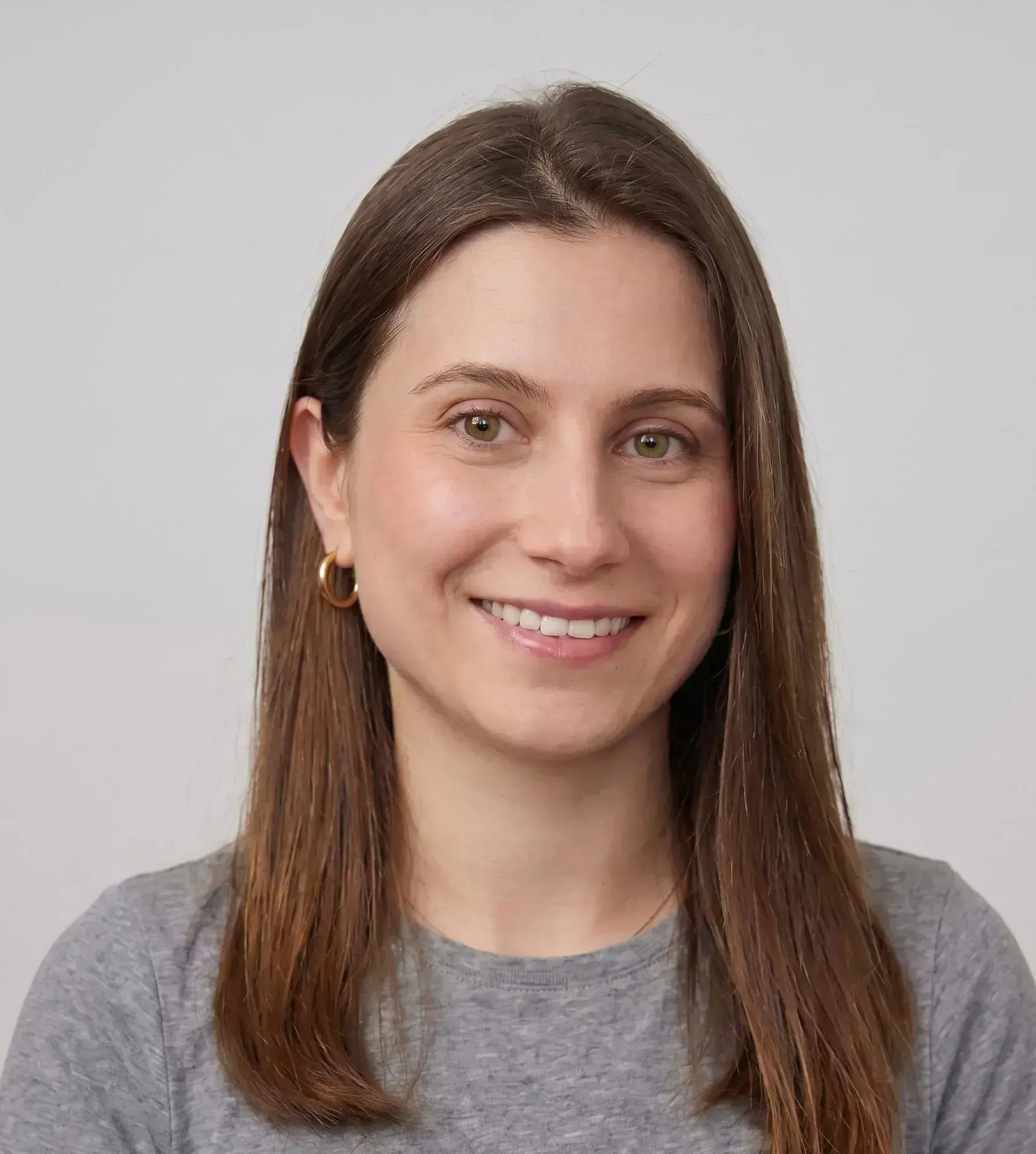 Portrait of a smiling woman with brown hair wearing a gray shirt on a plain background