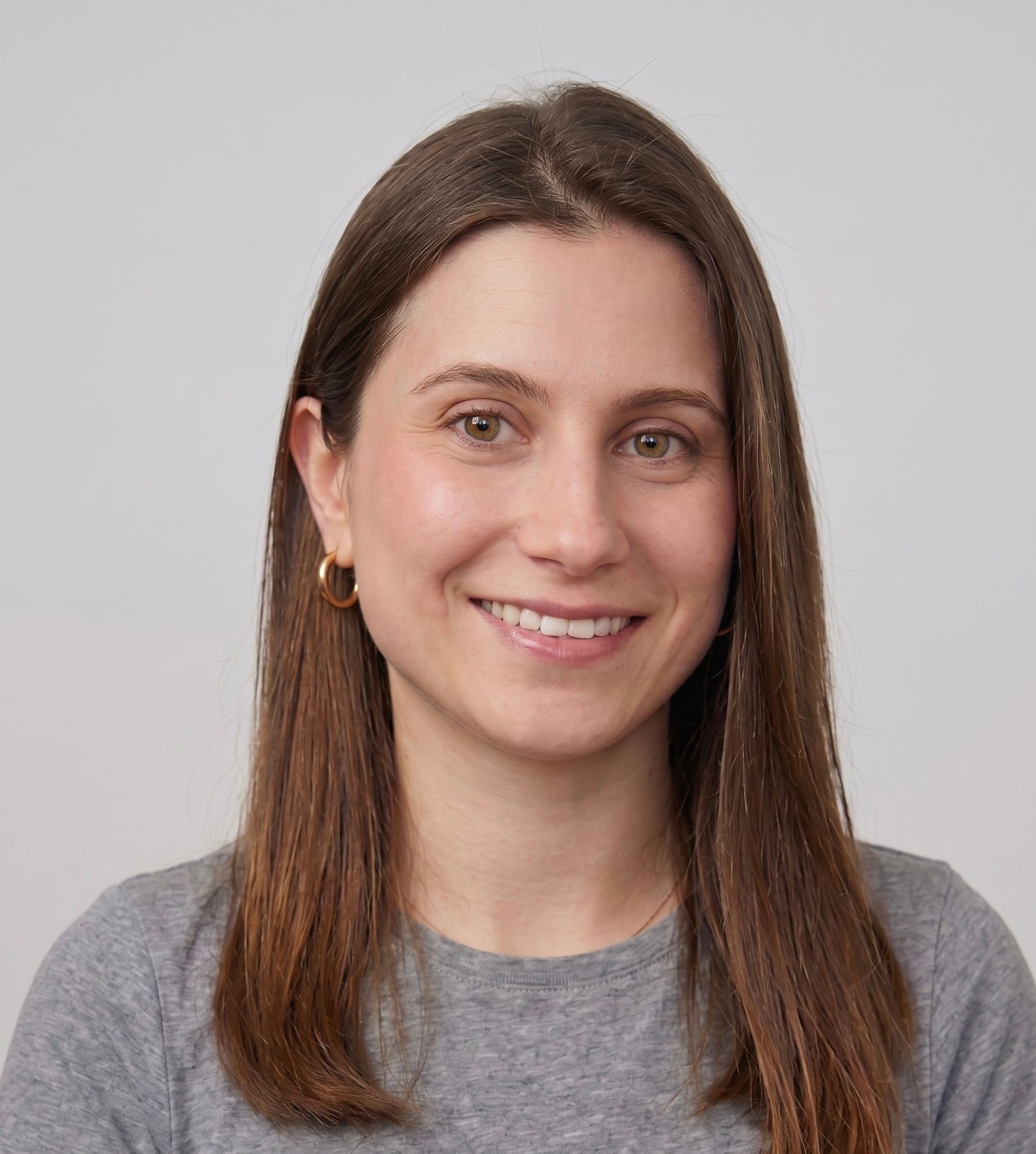 Portrait of a smiling woman with brown hair wearing a gray shirt on a plain background