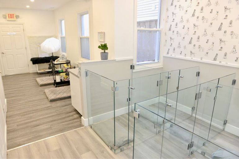 Bright hallway with glass railing, white walls, bench, potted plant, and exit sign near a doorway