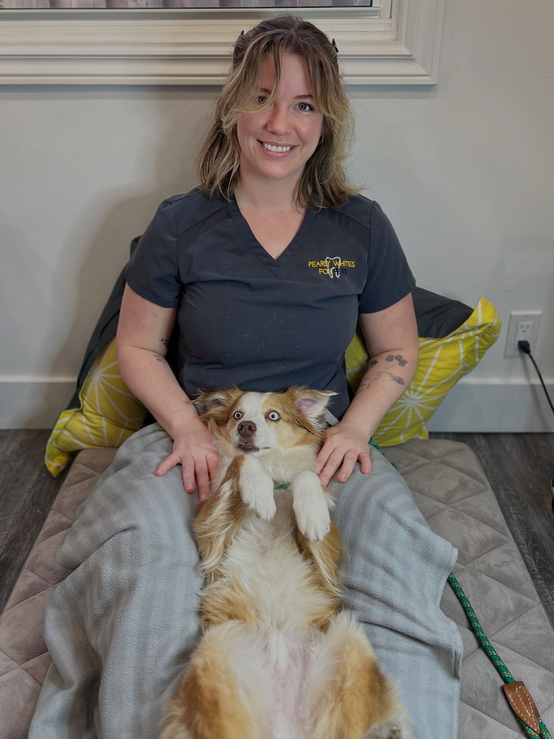 Woman smiling on a couch with a tan-and-white dog lying belly-up on her lap