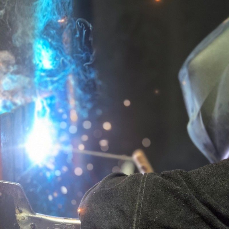 Welder in a protective helmet, welding with bright blue light and sparks.