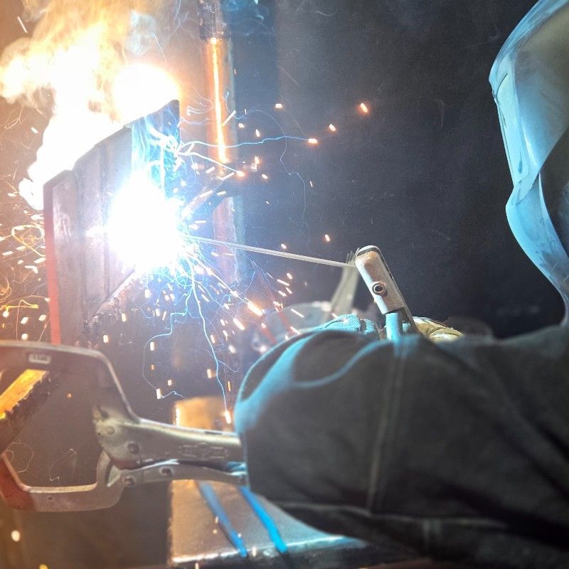 Person welding metal, bright sparks and light visible; dark setting.