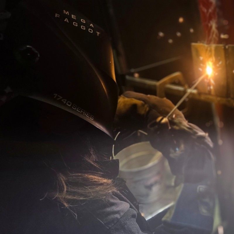 Person welding metal, wearing a helmet with the word 