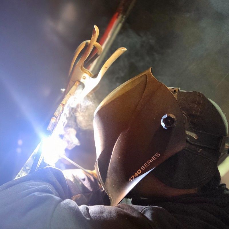 Welder in protective gear using a welding torch, sparks flying, working in a workshop setting.