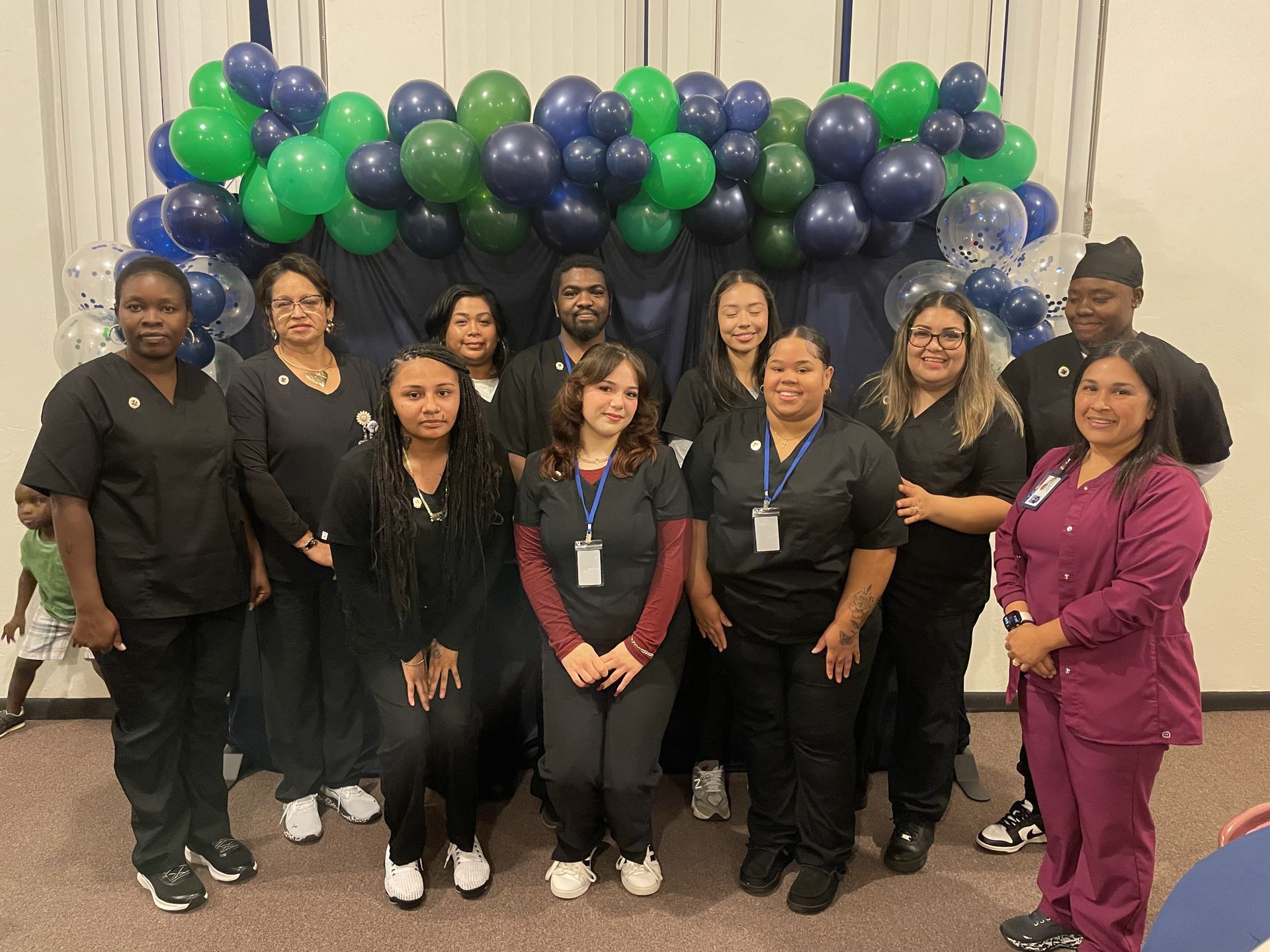 Group of people in scrubs pose under a balloon arch; some smile, in a room.