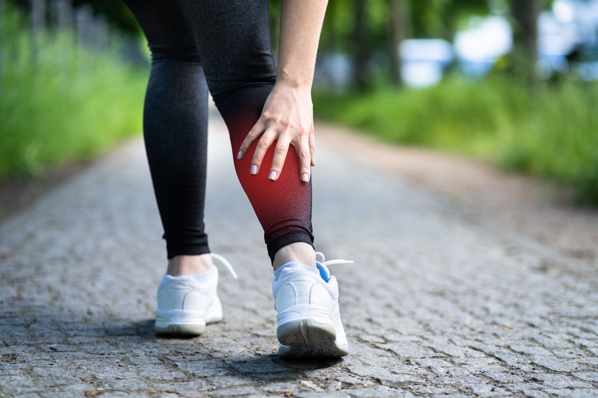 Person in black leggings clutching a red knee while walking on a paved path outdoors