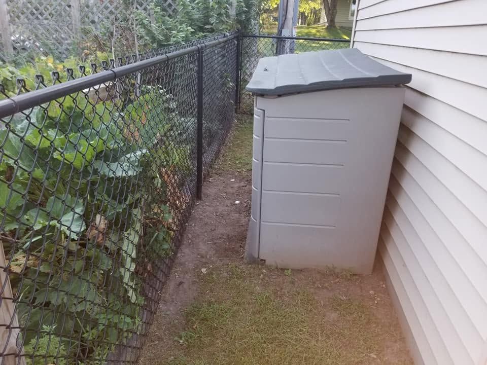 Narrow side yard with chain-link fence, gray storage bin, and white house siding.