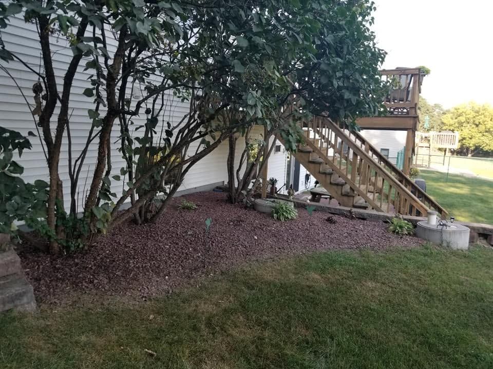 Backyard with grass, mulch bed, trees, and wooden stairs leading to a deck beside a house