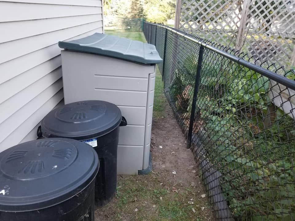 Backyard side yard with trash bins beside a house and a chain-link fence.